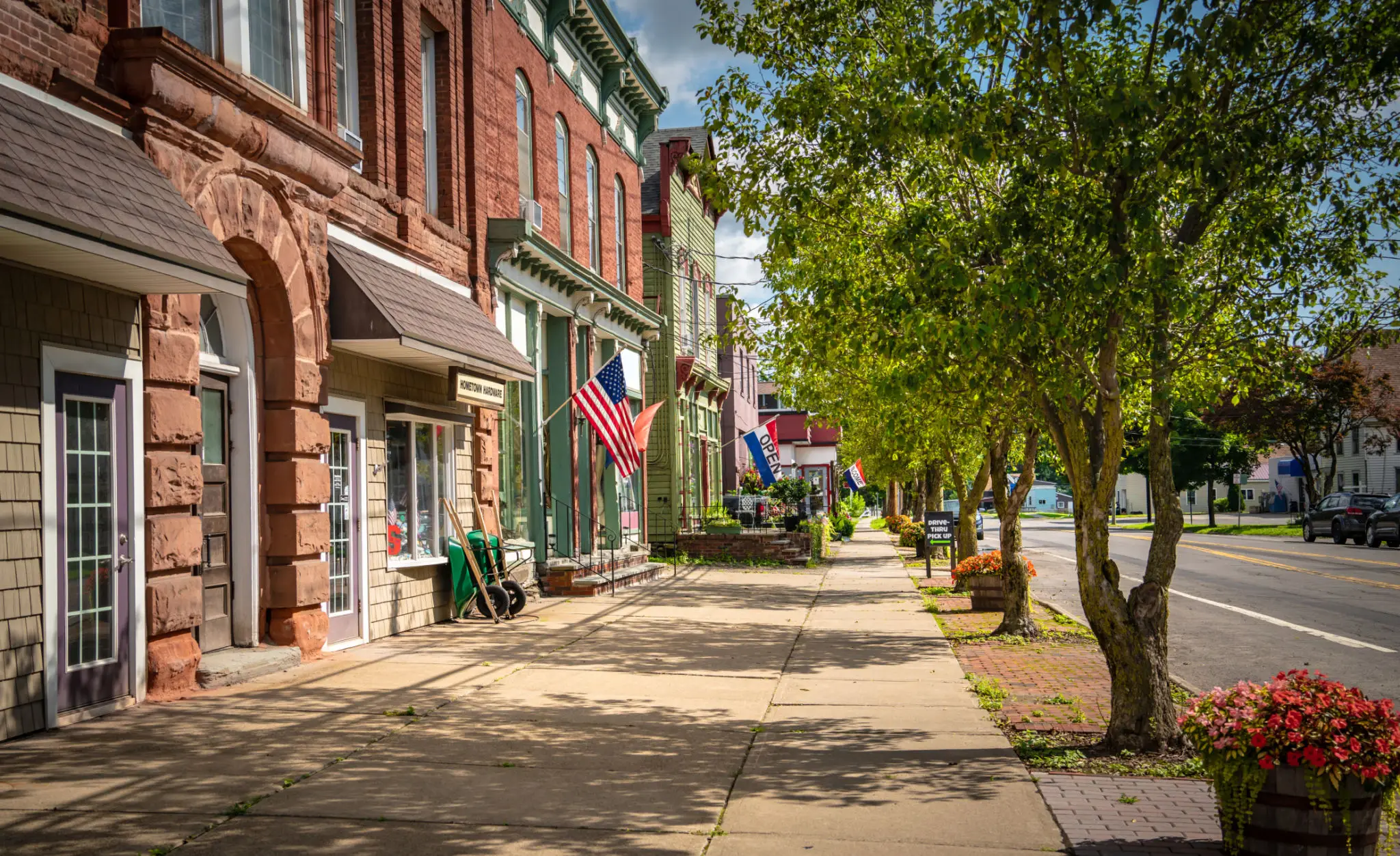 Quaint small-town street with American flags and trees lining the sidewalk.